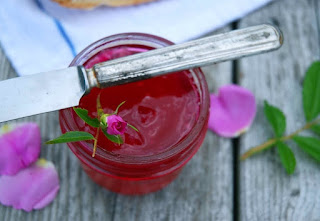 Rose petals surrounding glass jar of red jelly