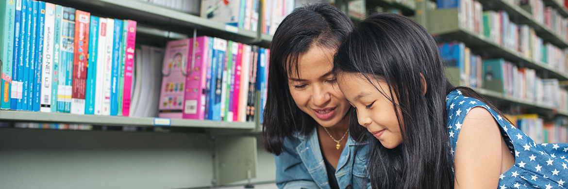 Mother and daughter in library, smiling while reading a book