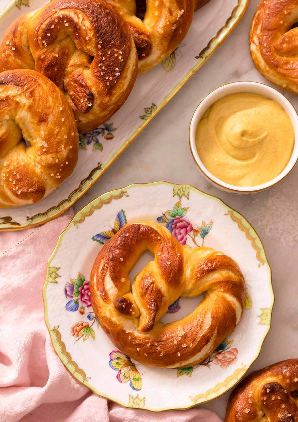 A soft pretzel on a plate next to a small dish of mustard. 