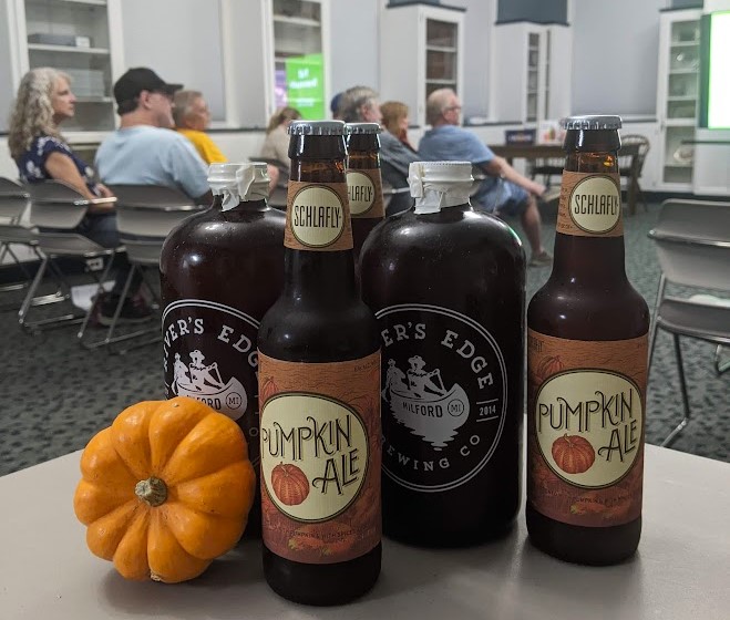 A variety of bottles and growlers of fall seasonal beers, with a mini pumpkin, in the Community Room during an Ale Together Now program. 