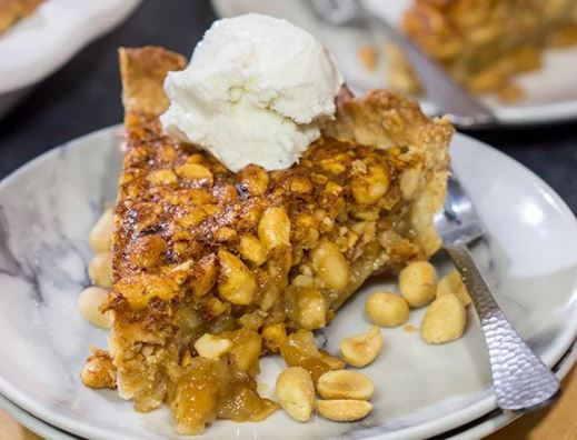 A plate with a slice of peanut pie, and a dollop of vanilla ice cream on top. 