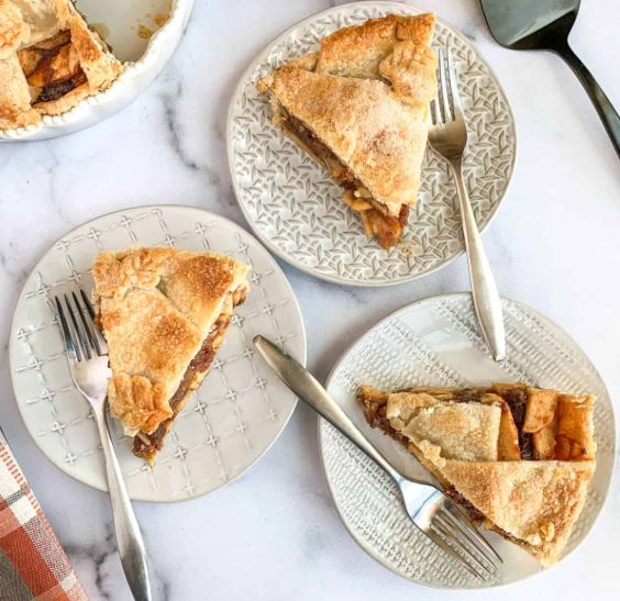 A top-view of apple date pie slices on individual plates with forks. 