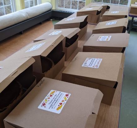 A table covered with pies in cardboard boxes, with Friends of CDL stickers on the top of each box. 