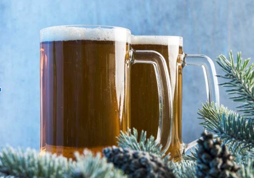 Two mugs of brown Jul beer, served in glass mugs with greenery and pinecones on the table. 