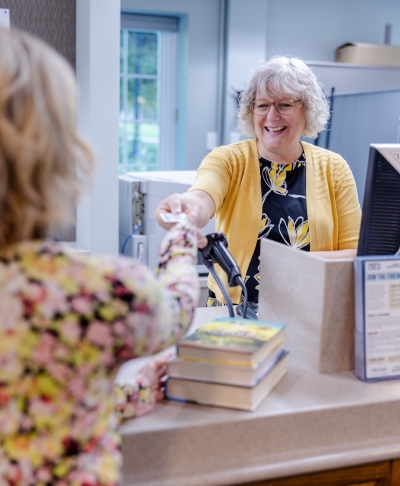 Circulation staff member handing a patron a Library card over the Circulation desk. 