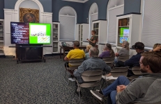 An audience sits classroom-style in the Community Room, watching Michelle give a presentation on Oktoberfest beers. 