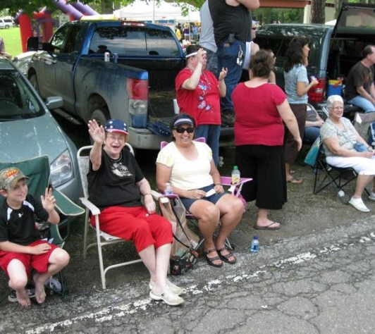 Hartland residents smiling and waving while sitting in lawn chairs at the Memorial Day parade