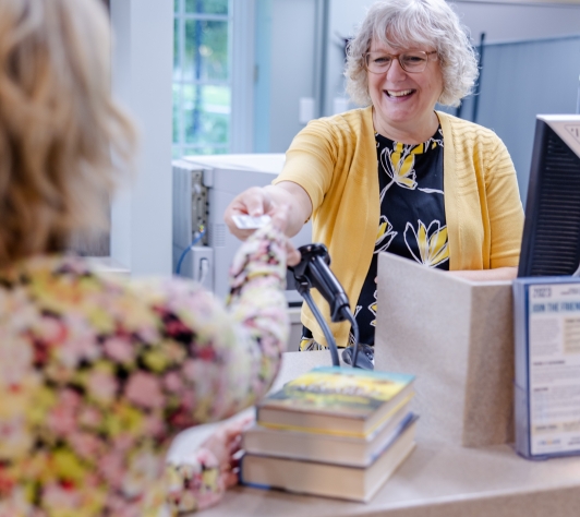 Circulation staff member handing a patron a Library card over the Circulation desk. 