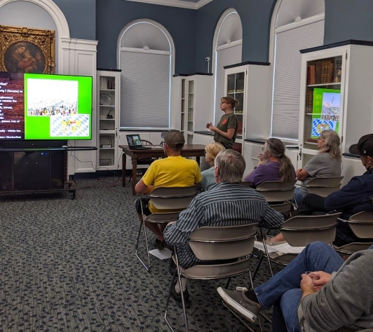 An audience sits classroom-style in the Community Room, watching Michelle give a presentation on Oktoberfest beers. 