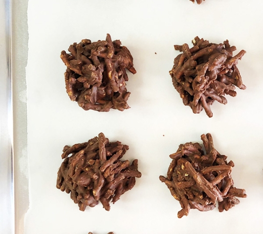 Eight no-bake chow mein cookies, lined up side by side in two rows on parchment paper. 