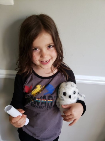 A child holding a rolled up Hogwarts letter and a snowy owl stuffie. 