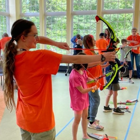 Teen volunteers and participants shooting toy arrows at targets at Percy Jackson Camp. 