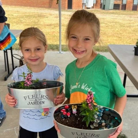 Two children showing off their hand-decorated flower pot fairy gardens. 