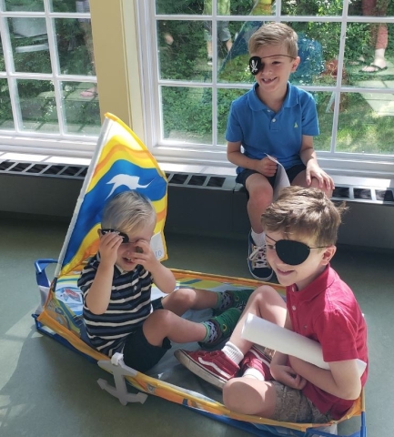 Children sitting in and near a makeshift pirate ship in the Youth Program Room. 