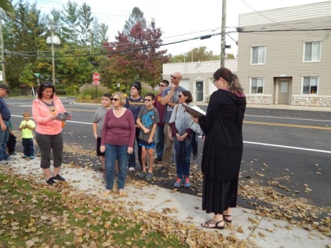 Librarian Carolyn reading a passage to a group of program attendees, on the sidewalk in the Hartland Village. 