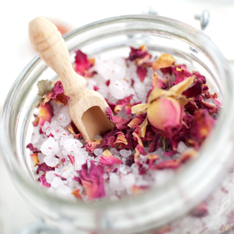 Bath salts, mixed with rose petals and other floral ingredients, with a small wooden scoop spoon. 