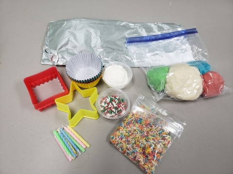 A variety of colors of playdough on a table with muffin cups, cookie cutters, colored rice, and other sensory items. 