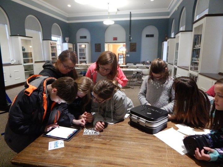 A group of tweens working at a table to decipher a code, with a lockbox on the table beside them. 