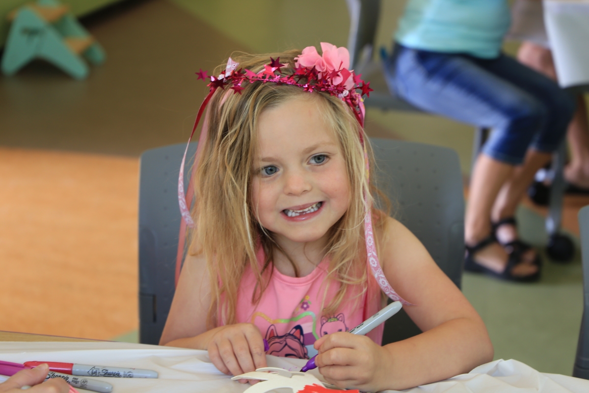 A young girl with a pink tiara coloring in the Youth Program Room. 